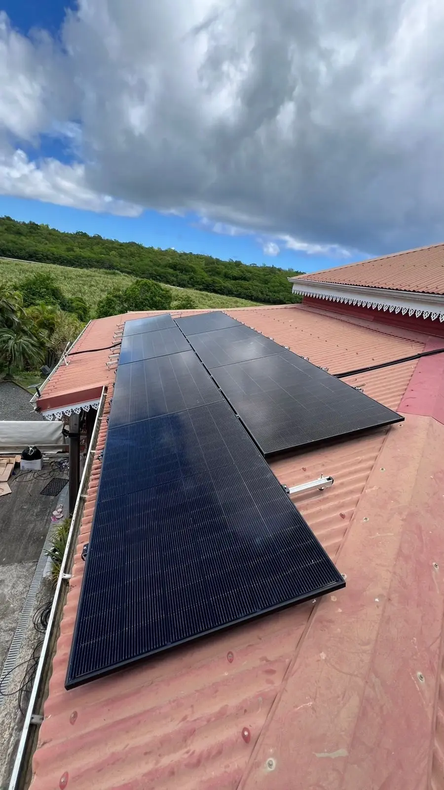 Deux rangées de panneaux photovoltaïques sur le toit d’une maison créole à lambrequins, face aux mornes